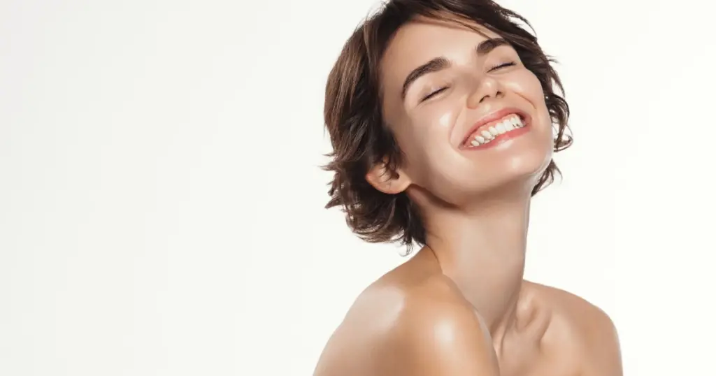 A smiling woman with short hair poses with closed eyes and glowing skin against a light background, representing peptide therapy in Highland, MD.